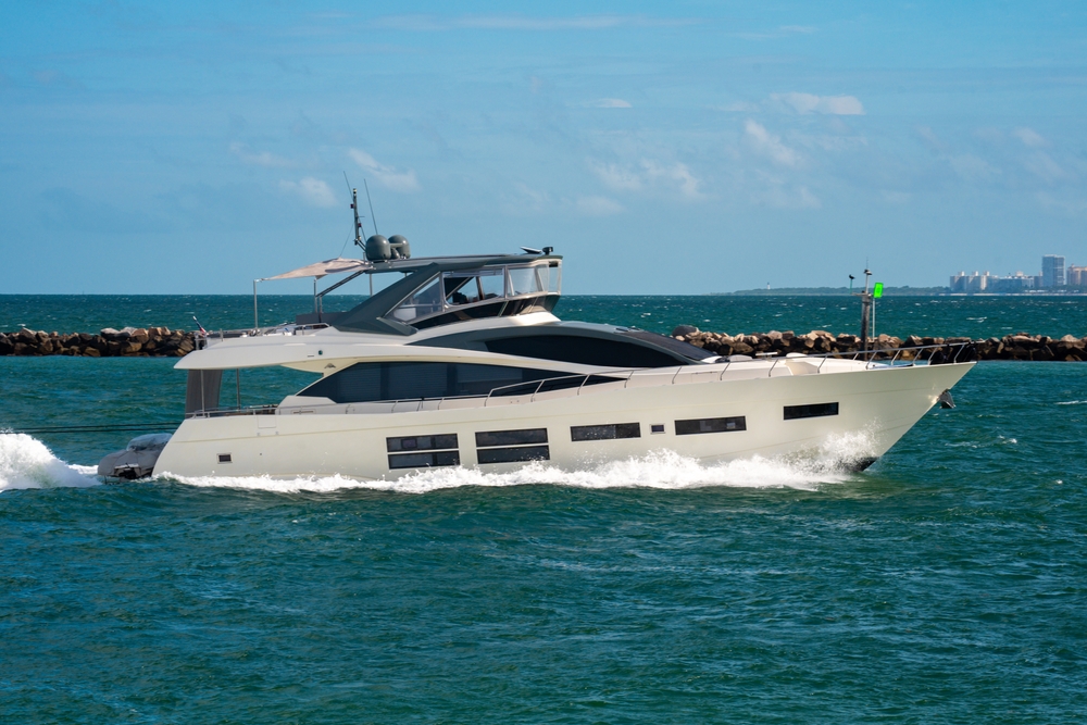 A modern white yacht with large windows cruises through blue-green water near a rocky breakwater under a partly cloudy sky, not far from NY’s skyline—where luxury vehicle storage in Nassau & Suffolk County is sought after by discerning yacht owners.